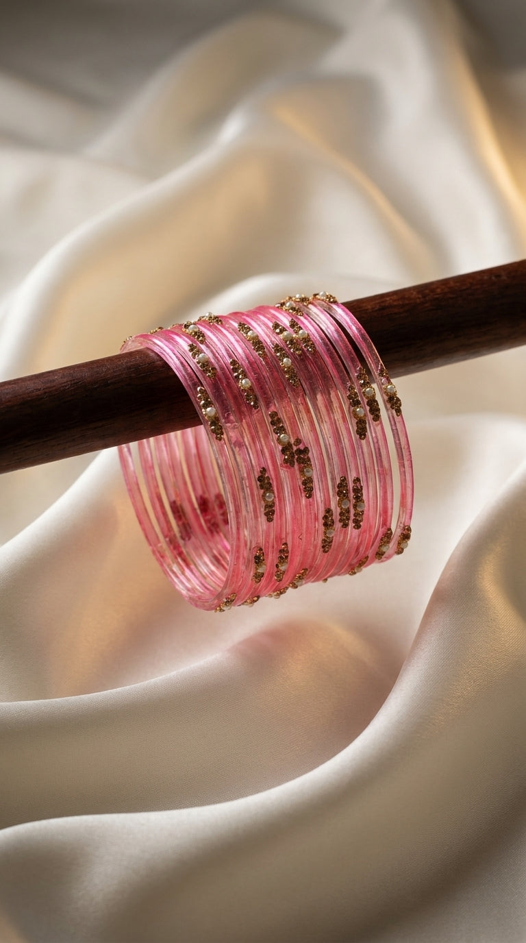 Pink glitter bangles stack with gold detailing and pearl-style beadwork draped on a wooden rod