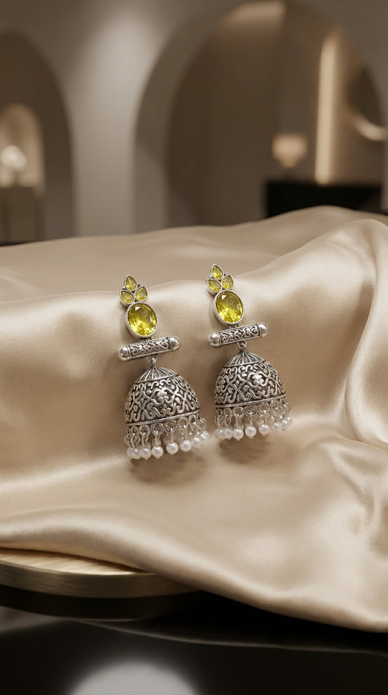 Oxidised silver dome jhumka earrings with yellow faceted stones and white pearl drops, displayed on cream satin — Behuli