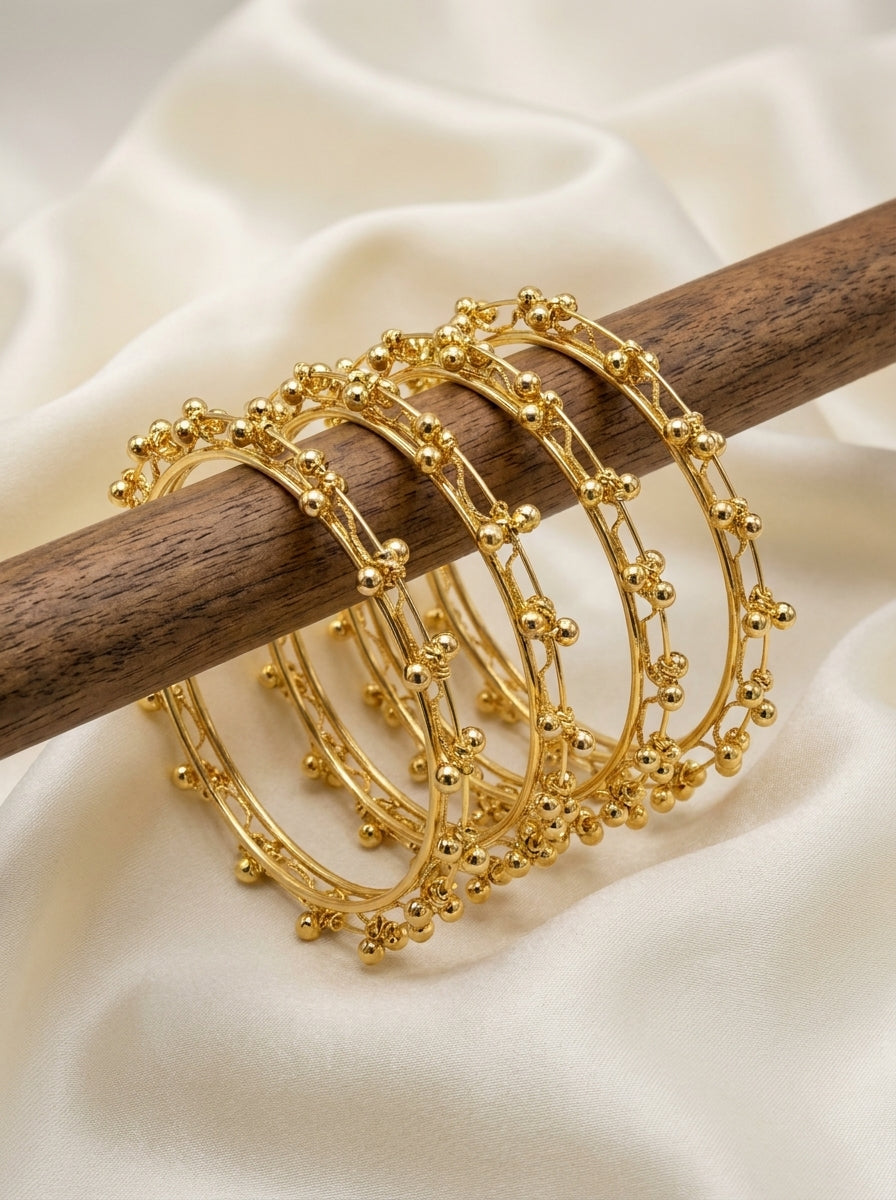 Set of four gold-plated ghungroo beaded bangles displayed on a wooden rod against ivory silk — Behuli Australia