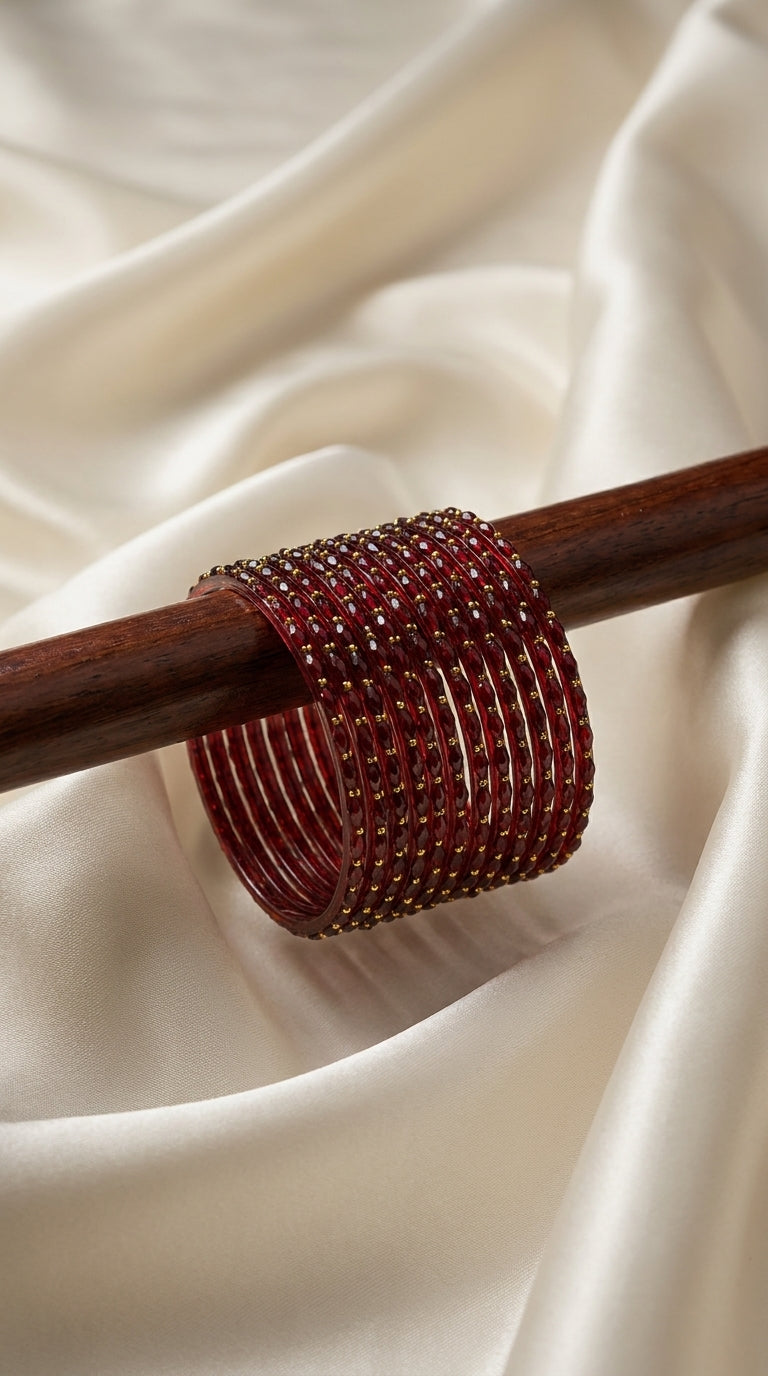 Set of 12 deep crimson red bangles with gold bead detailing stacked on a wooden display rod — Behuli Australia