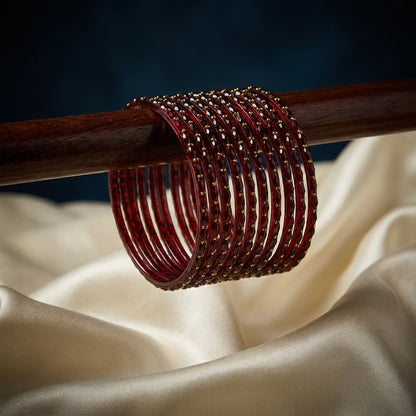 Set of 12 deep crimson red bangles with gold bead detailing stacked on a wooden display rod — Behuli Australia — view 2