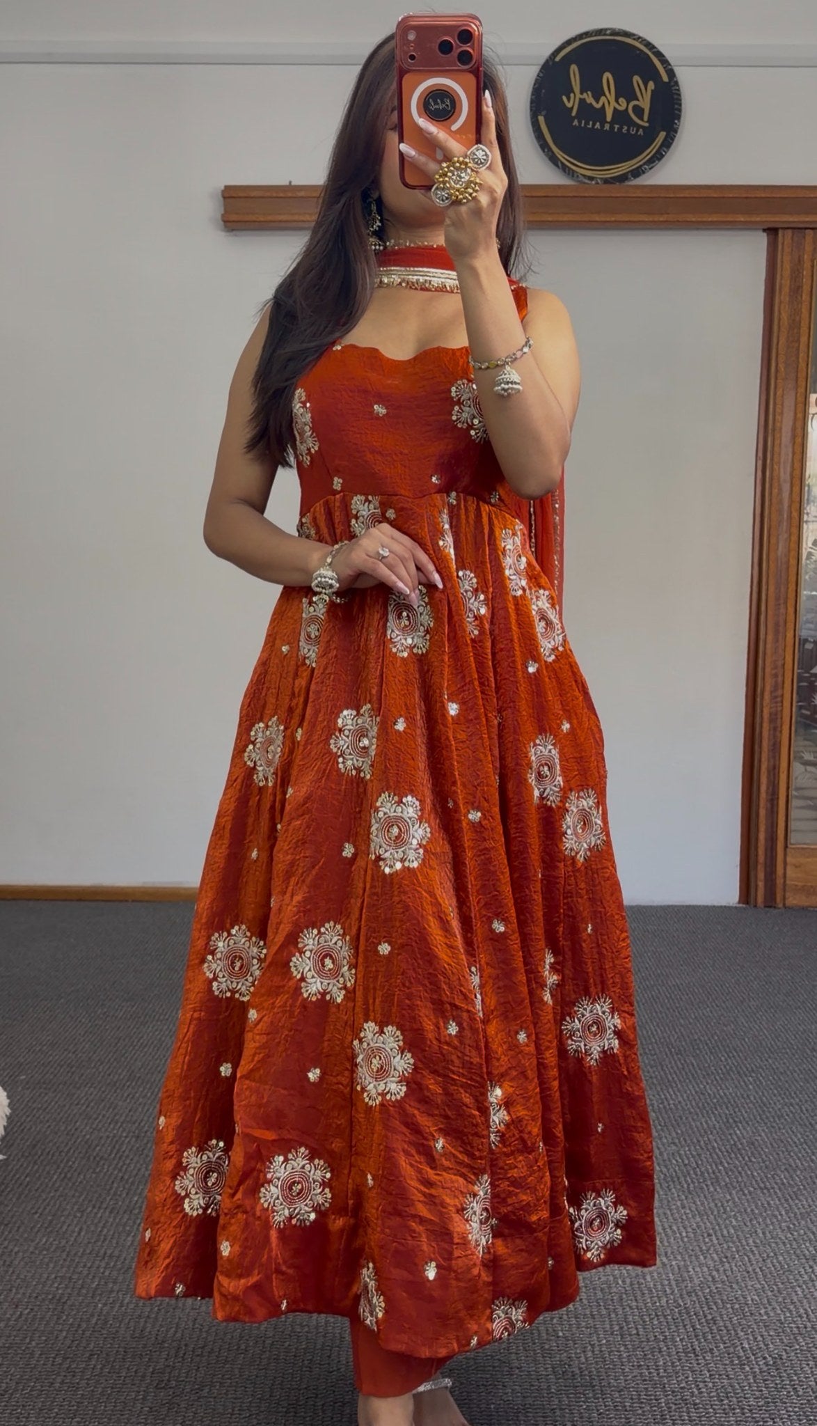 Rust orange Anarkali gown with ivory and gold circular floral embroidery, styled with gold choker and jhumka earrings —