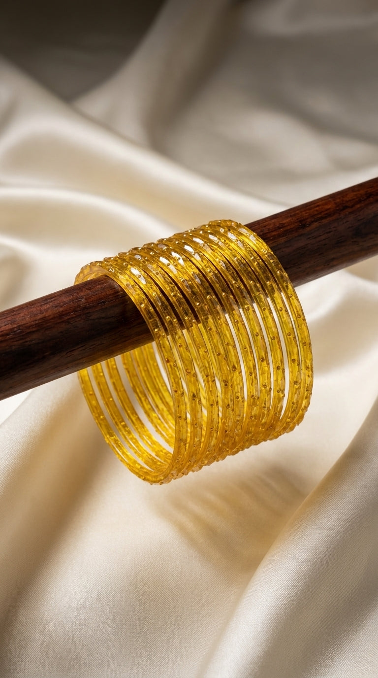 Set of 12 golden yellow glitter-finish bangles stacked on a dark wooden rod against ivory silk — Behuli Australia