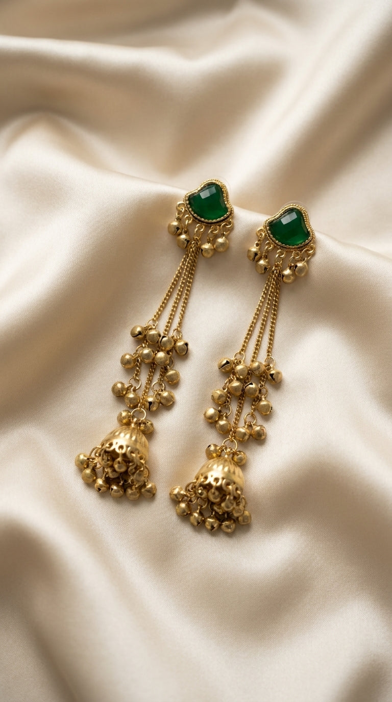 Gold-tone long drop jhumka earrings with faceted green stone, ghungroo bell clusters and chain tassels on cream silk —