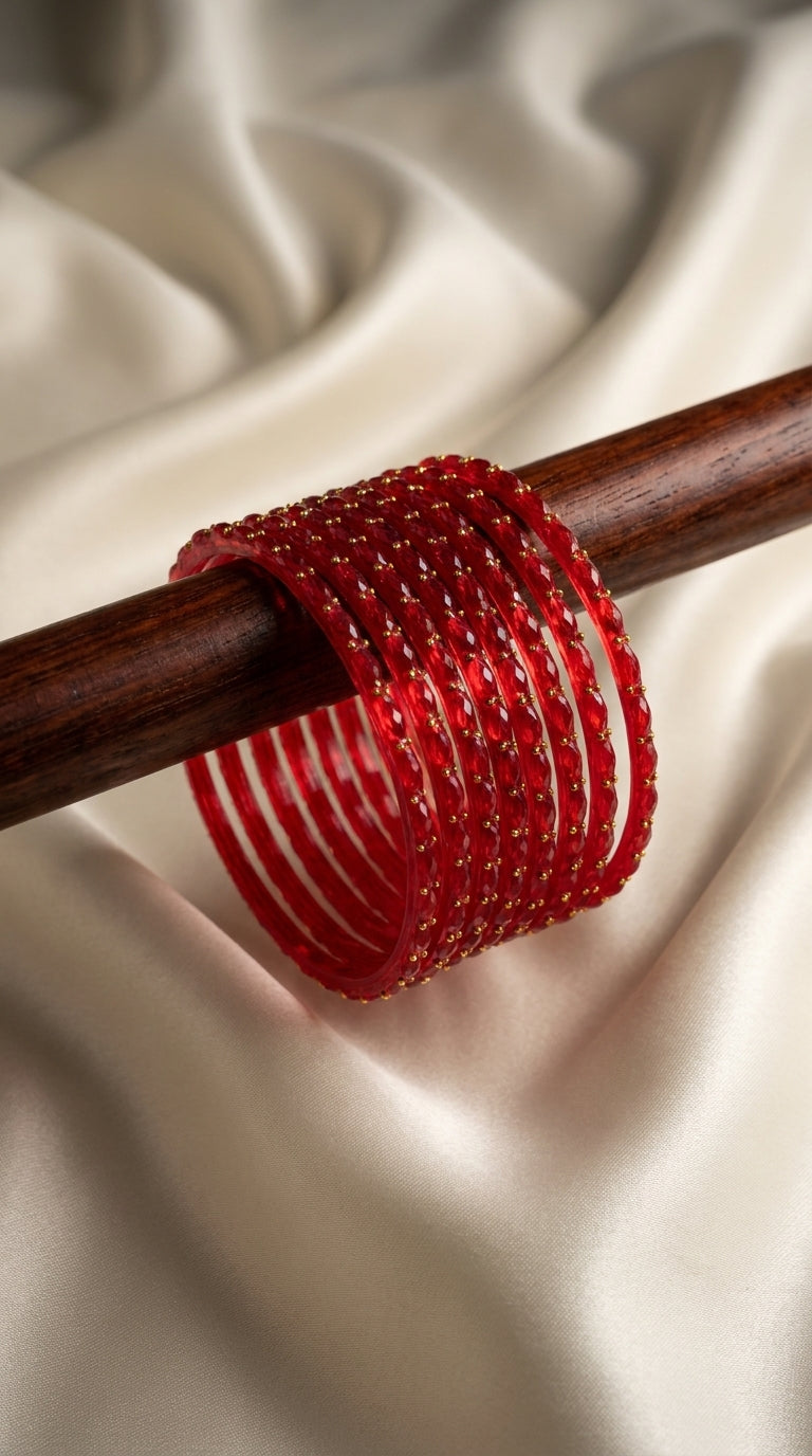 Red bangles stacked with gold bead detailing on a wooden rod against ivory satin fabric — Behuli Australia