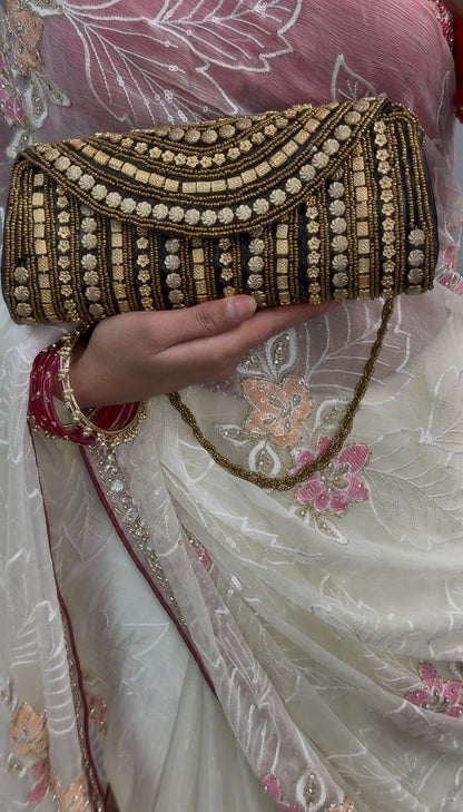 Black clutch bag with gold beadwork and sequin detailing, featuring a beaded chain strap, displayed on wooden table — view 2