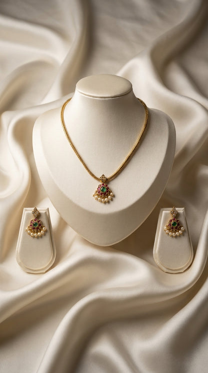 Gold-tone necklace and earring set with red and green stone embellishment and pearl drops displayed on ivory jewellery bust