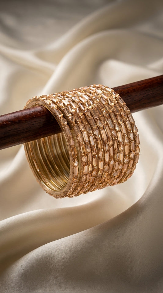 Set of six gold-toned bangles with champagne stone embellishments stacked on a wooden rod against ivory silk fabric