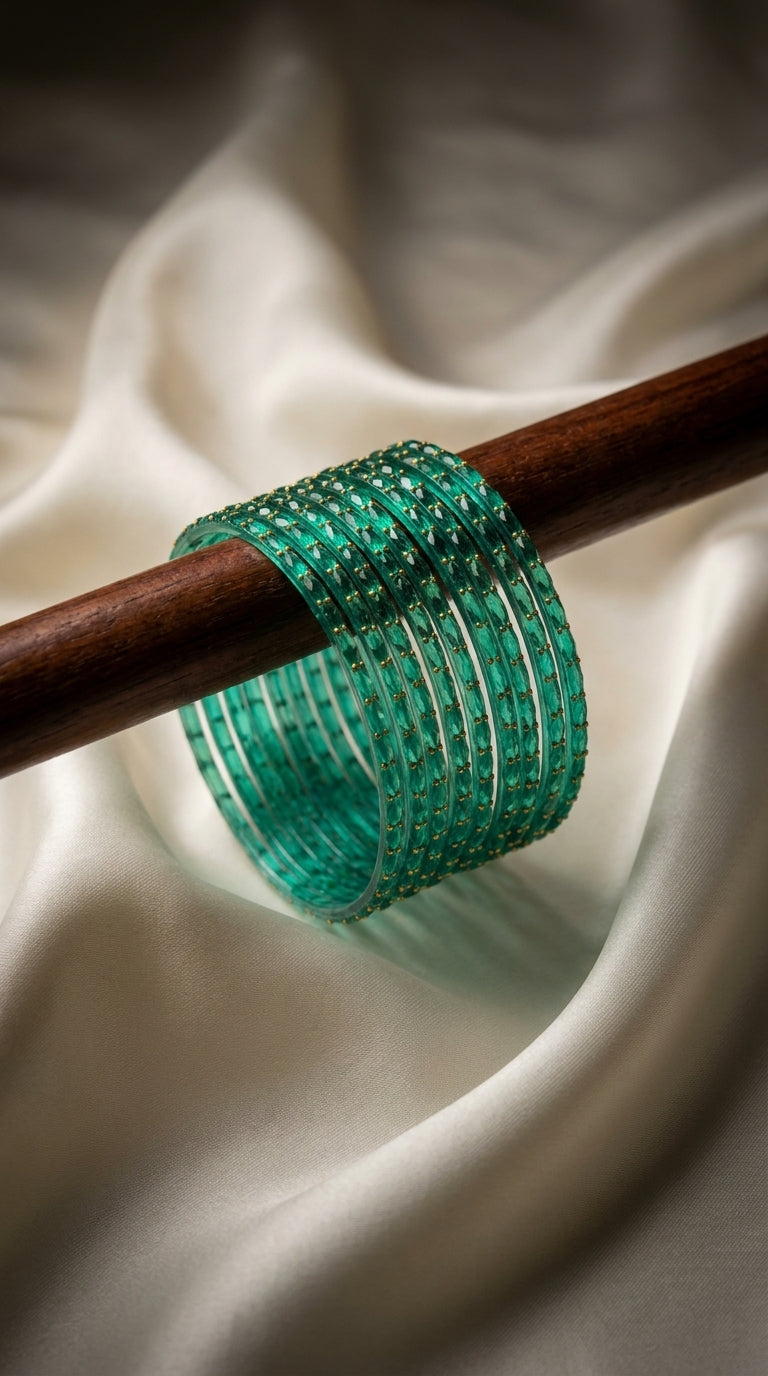 Stack of teal green bangles with sparkling stone embellishment displayed on a wooden rod with ivory fabric background