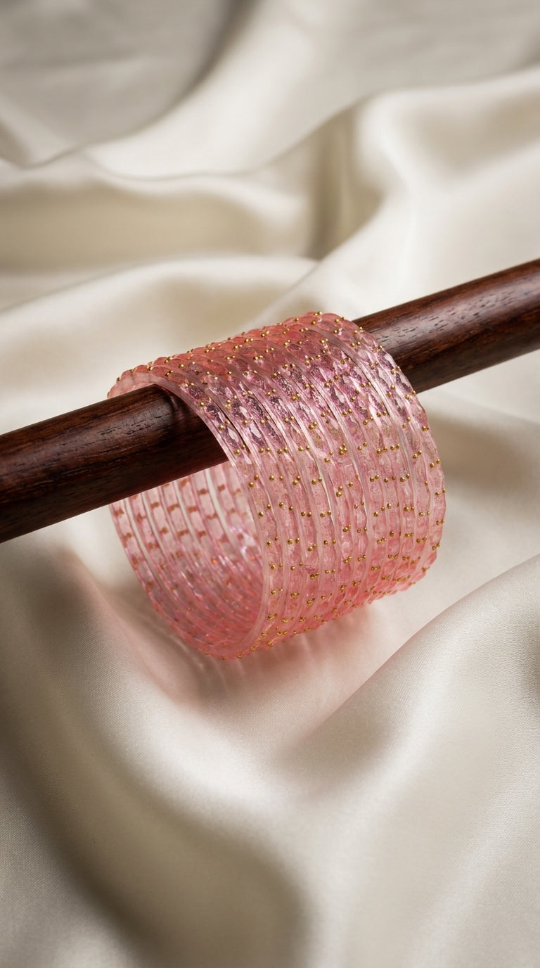 Set of 12 blush pink translucent bangles with gold-toned bead detailing displayed on a wooden rod — Behuli Australia