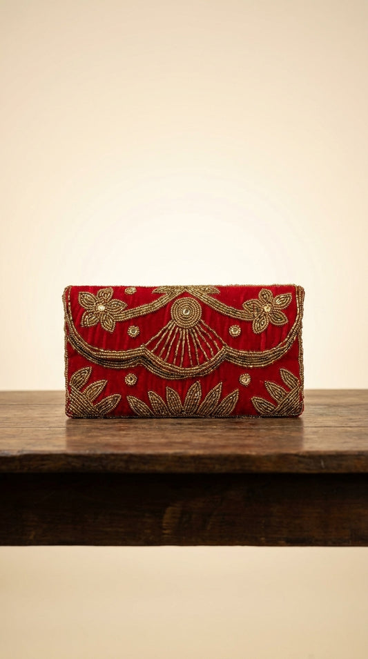 Red velvet-look clutch bag with gold beadwork floral and leaf embroidery detailing on wooden display shelf
