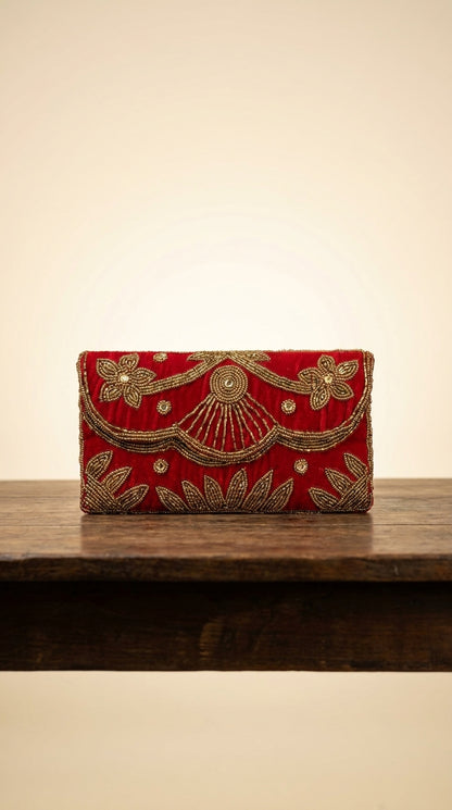 Red velvet-look clutch bag with gold beadwork floral and leaf embroidery detailing on wooden display shelf