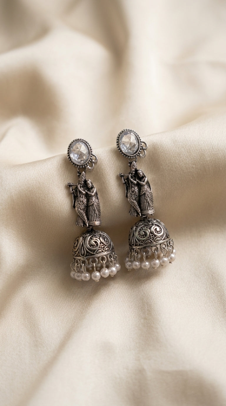 Oxidised silver Radha Krishna jhumka earrings with filigree dome bell and white pearl drops on ivory fabric — Behuli