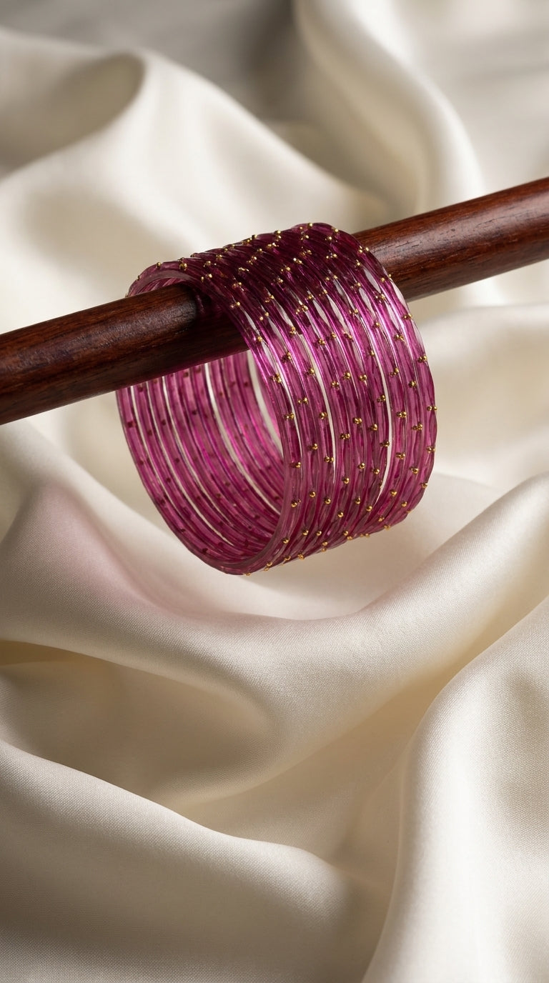 Set of 12 fuchsia bangles with gold-tone dot accents displayed on a wooden rod over ivory silk — Behuli Australia