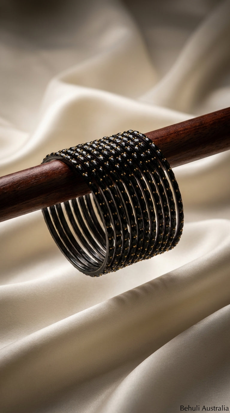 Set of 12 black bangles with gold bead detailing stacked on a wooden rod against ivory satin fabric