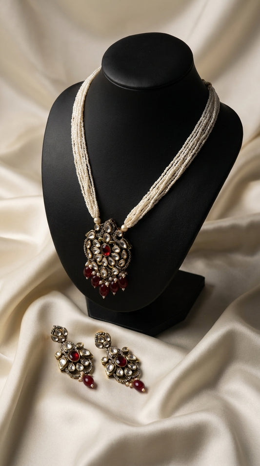 Ivory pearl beaded necklace set with gold Kundan-style pendant and maroon drop embellishments, matching earrings displayed